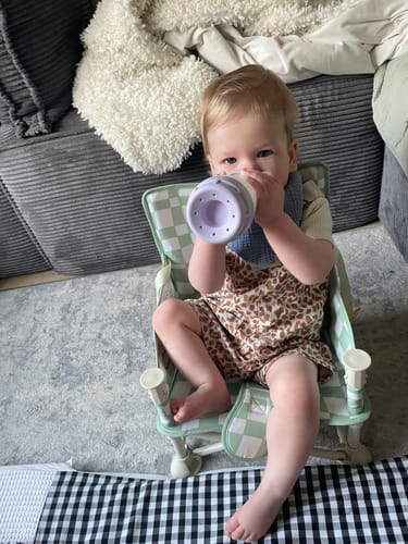 Customer's baby sits in the green checkered Parker baby chair, drinking from a bottle.