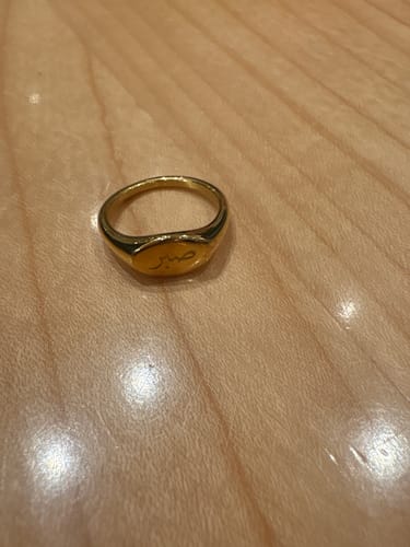 Customer's engraved gold Patience Ring on a light wooden surface.