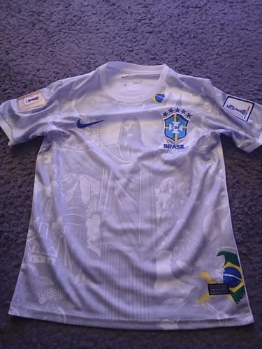 Un client montre son maillot spécial Brésil blanc posé à plat, affichant le design avant complet sur un tapis.