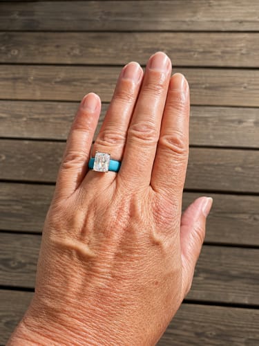 A reviewer's hand wearing the Silicone Ring in ocean color with a large, emerald-cut CZ stone.