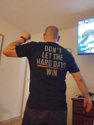 Reviewer from behind flexing in a black Hard Days shirt showing the text 'Don't Let The Hard Days Win'.