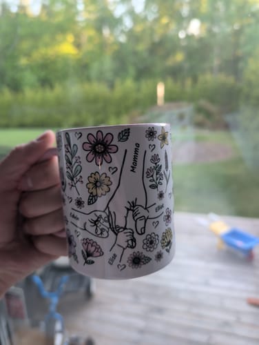 En kund håller i sin personliga Kärleksmugg med en illustration av händer, blommor och namn.