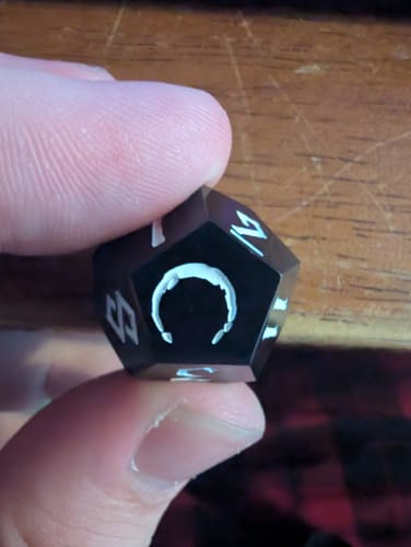 Close-up of a customer holding a black d12 die from the Darkest Dungeon set, showing a flawed and uneven symbol.