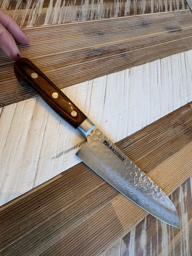 Customer's Hanmā Santoku knife on a wooden surface, showing its patterned blade and dark handle.
