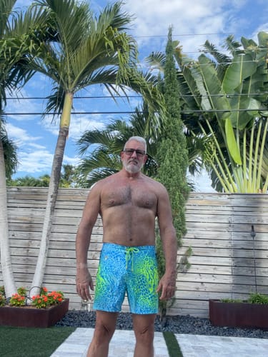 Reviewer standing outdoors wearing the bright, patterned Vivid Jungle swim trunks.