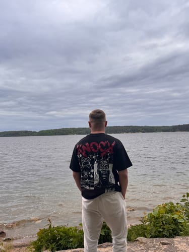 Customer wearing the black oversized EMBRACE THE STRUGGLE 2.0 TEE from behind, standing by a lake.