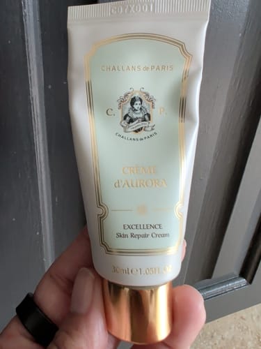 Reviewer holding the white and gold tube of Challans de Paris Crème d'Aurora moisturizer.