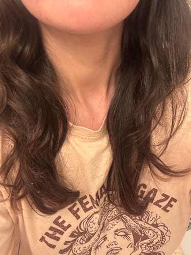 Cliente montrant le résultat du lissage brésilien sur ses cheveux bruns, qui restent ondulés.