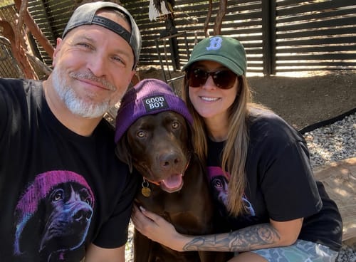Customers wearing matching black Night Watch t-shirts while posing with their dog outdoors.