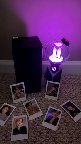 A reviewer's BTS Official Light Stick Ver. 4 glows purple next to its box, with several photocards arranged on the floor.