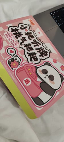 Reviewer's pink boxset for the Small PA Waiting for the Tile blind bag, shown on a white surface next to a laptop.