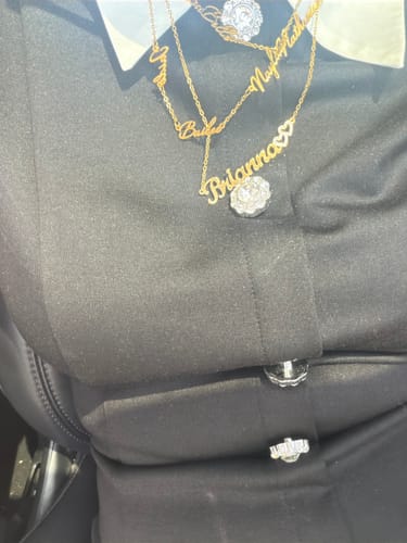 Close-up of a reviewer wearing several layered gold Iced Hearts Name Necklaces over a black shirt.