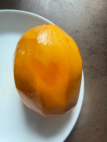 Kundenbild einer leuchtend orangen, geschälten Mango Mingolo auf einem Teller.