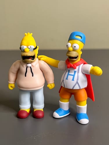 Reviewer's Dancin Homer figure with a red cape, posed next to another Homer Simpson figure on a table.