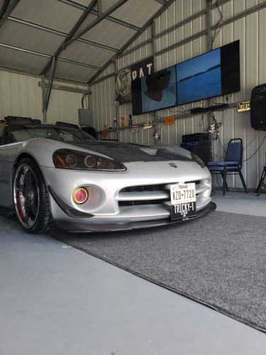 Customer's Texas Blackout Metal License Plate with custom text 'TRICKY-1' on the front of a silver sports car in a garage.
