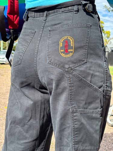 Close-up: Customer wearing black Construction Pants, showing the high waist and back pocket with logo patch.