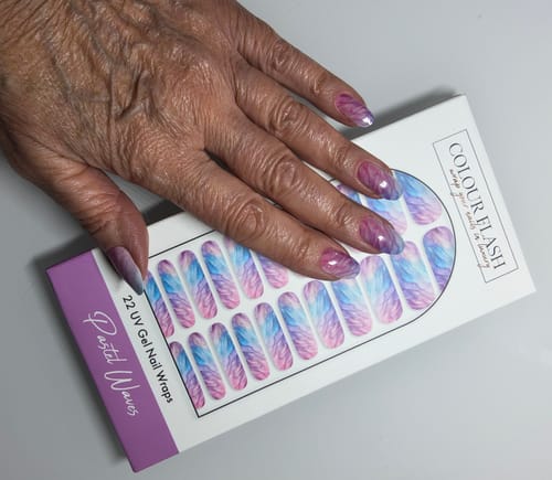 Hand einer Kundin mit aufgetragenen 'Pastel Waves' UV Gel Wraps, die auf der Produktverpackung liegt.
