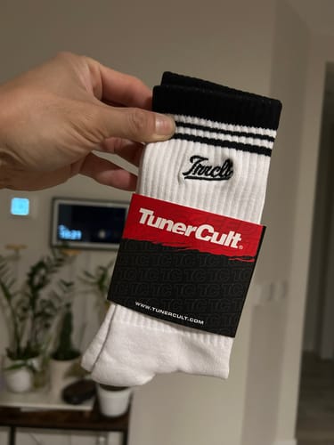 Customer's hand holding a new pair of white SCRIPT CREW SOCKS in their packaging.