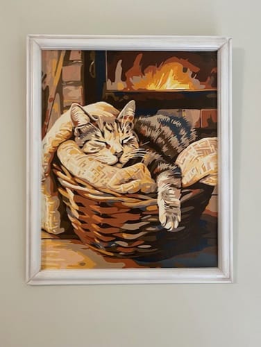 Reviewer's completed Bascat painting of a cat sleeping in a basket, framed and hanging on a wall.