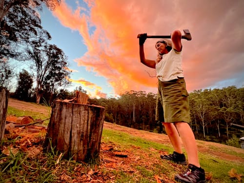 Reviewer wearing the hunter green Long Shorts while chopping wood in a rural setting at sunset.