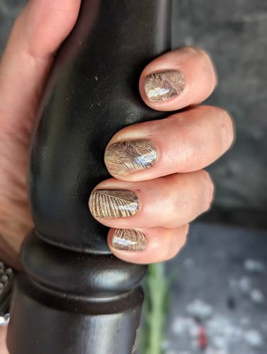 Kundenhand mit aufgetragenen 'Festive Palms' Nagelfolien, die ein detailliertes, goldenes Palmblatt-Design zeigen.