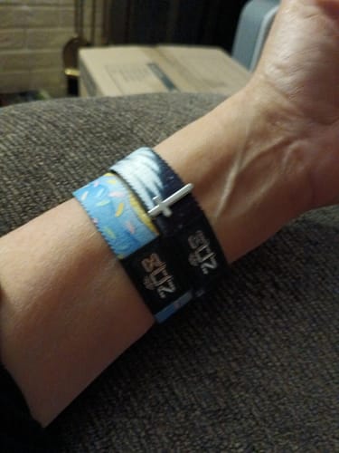 Customer wearing the light blue Happy Birthday Bracelet on their wrist next to another dark bracelet.