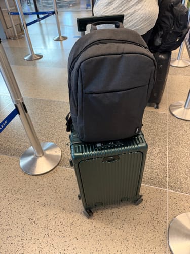 Customer's green All-in-One Expandable carry-on suitcase at an airport, with a backpack resting on its handle.