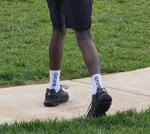 Customer walking on a sidewalk, showing a rear view of the white socks and black shoes.