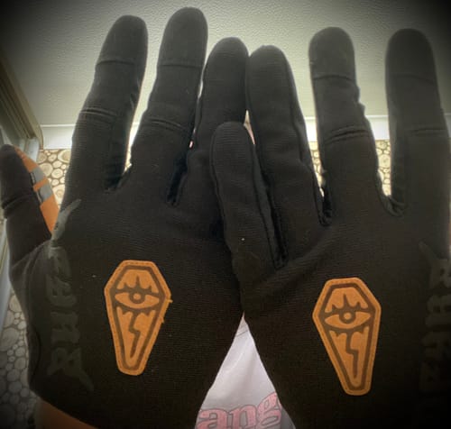 Reviewer holds up both hands, showing the back of the black Wraith | Gravity Gloves with their orange coffin logos.