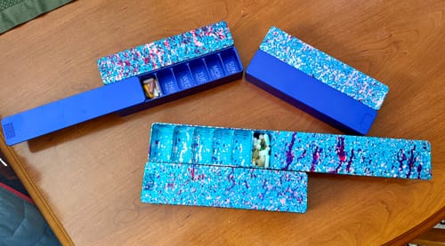 Customer's three blue and speckled 2-Week Vitamin XL Cases on a wooden table. Two cases are open showing pills inside.