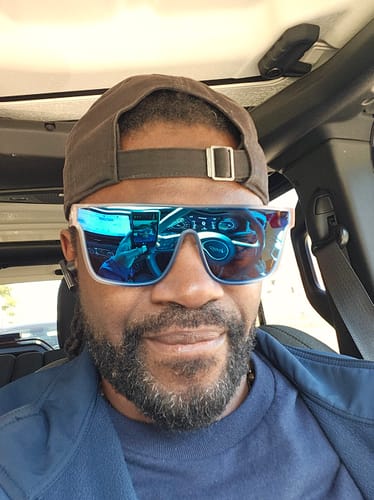 Reviewer smiling while wearing the blue, reflective 80Eighty Polarized Murica Sunglasses in a car.