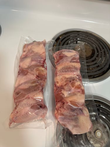 Customer's two vacuum-sealed packages of raw meat cuts resting on a stovetop.