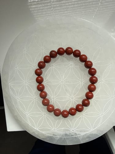 Un client montre son bracelet en jaspe rouge de 8 mm posé à plat sur une plaque décorative blanche.
