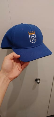 Reviewer holding their royal blue baseball cap, showing the custom embroidered logo with a crown and shield.