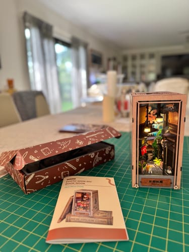 Customer's finished Kyoto Gion Book Nook Kit, lit up and displayed on a green mat next to the instruction manual and box.