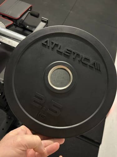 Ein Kunde hält eine schwarze 2,5 kg Gummi-Hantelscheibe in der Hand, um die Oberfläche und die Verarbeitung zu zeigen.