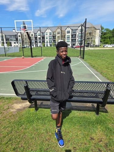 Customer wearing the 'Lion' Youth Performance Shorts and a hoodie at an outdoor basketball court.