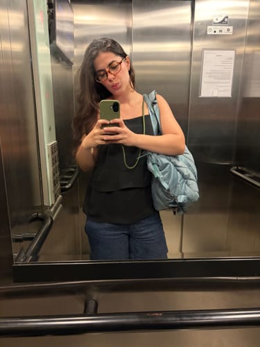Avaliadora tirando uma selfie no espelho, mostrando sua Case Verde Musgo com alça em um celular.