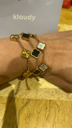 Customer's wrist, showing three Celine Clover Bracelets in gold, black, and white mother of pearl styles.