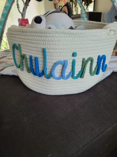 Customer's personalized knitted basket with the name "Chulainn" in multicolor yarn, filled with toys.
