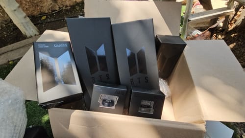 Reviewer's open shipping box revealing multiple packages for the BTS Official Light Stick Ver.4 and Cradle.
