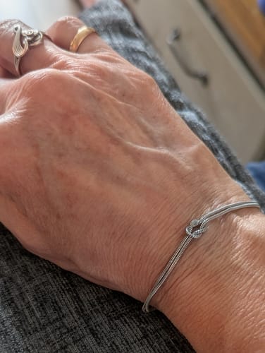Close-up of a customer's wrist wearing the elegant Forever Knot Bracelet against a dark fabric background.