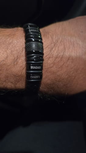 Close-up of a customer's personalized black bracelet on their wrist, engraved with the names 'Isaiah' and 'Daisy'.