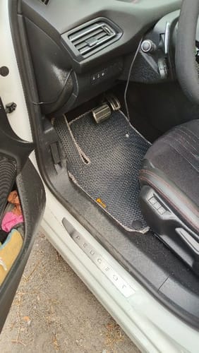 Recenzent pokazuje dopasowaną, czarną matę podłogową po stronie kierowcy w samochodzie.