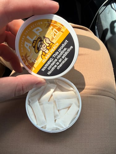 Reviewer holding an open can of Drifters Island Peach Nicotine Pouches, revealing the white pouches inside.