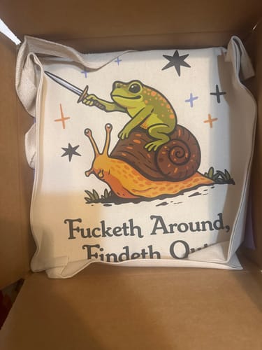 Reviewer's "Fucketh Around, Findeth Out" tote bag with a funny frog design, shown carefully packed in a shipping box.