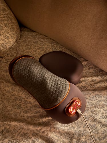 Customer's purple Thera Pillow on a patterned bed sheet, plugged in with its control buttons illuminated in red.