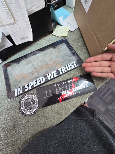 Customer's INTERNATIONAL SLAP sticker displayed on the floor with a matching license plate frame and a round decal.