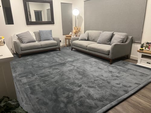 Customer's large, dark grey Mellow Mat covering the floor of a lounge room with two grey sofas.