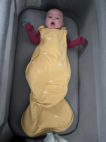 Customer's baby wearing the yellow, sun-patterned Ultimate Baby Sleep Bag in a bassinet.